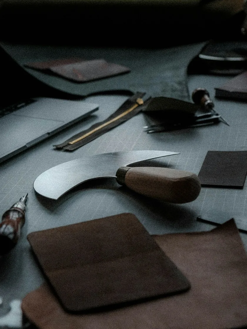 Outils de maroquinerie disposés sur un établi : lames, alênes, poinçons et petits accessoires de coupe
